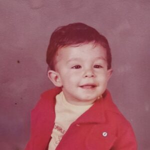 Toddler photo of Gregory G. Camacho smiling in a red jacket